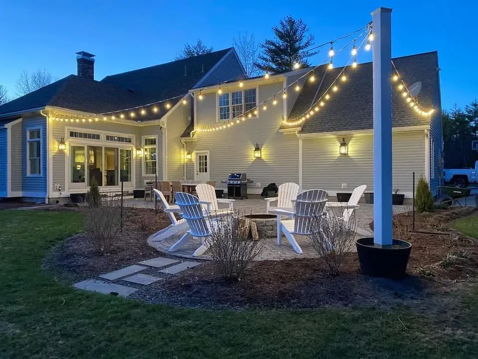 Bistro string lights hung from a black pole over a fire pit patio at dusk