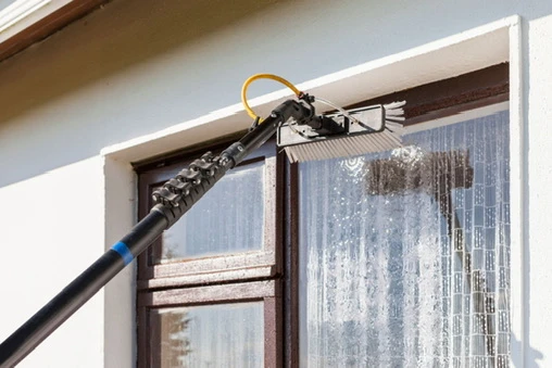 Water-fed brush washing a window with water running down the glass