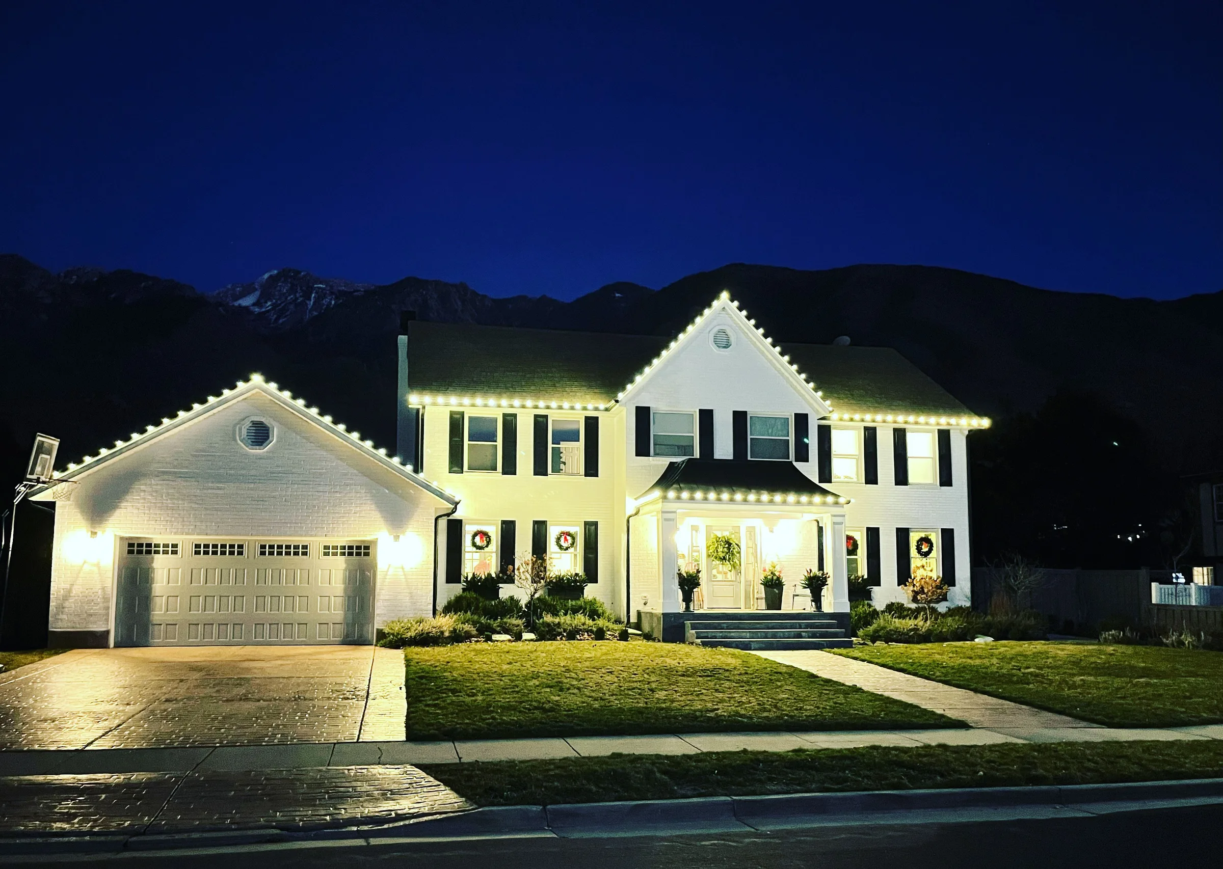 Colonial home outlined in warm white below the mountains