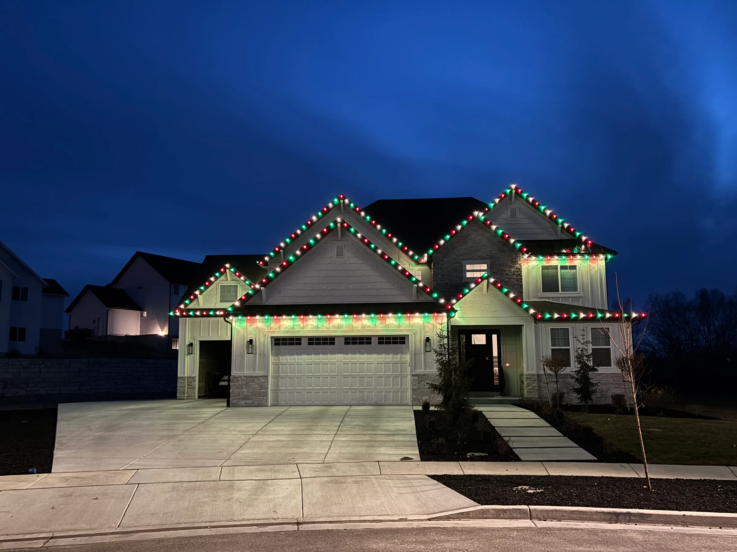Two-story craftsman home outlined in red and green roofline lights