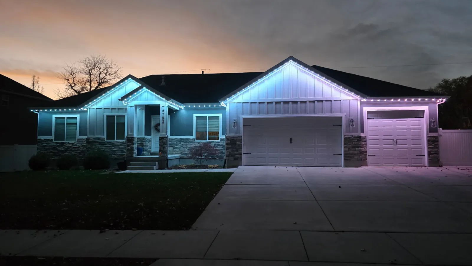Single-story home at dusk with roofline lights glowing blue and pink across every gable