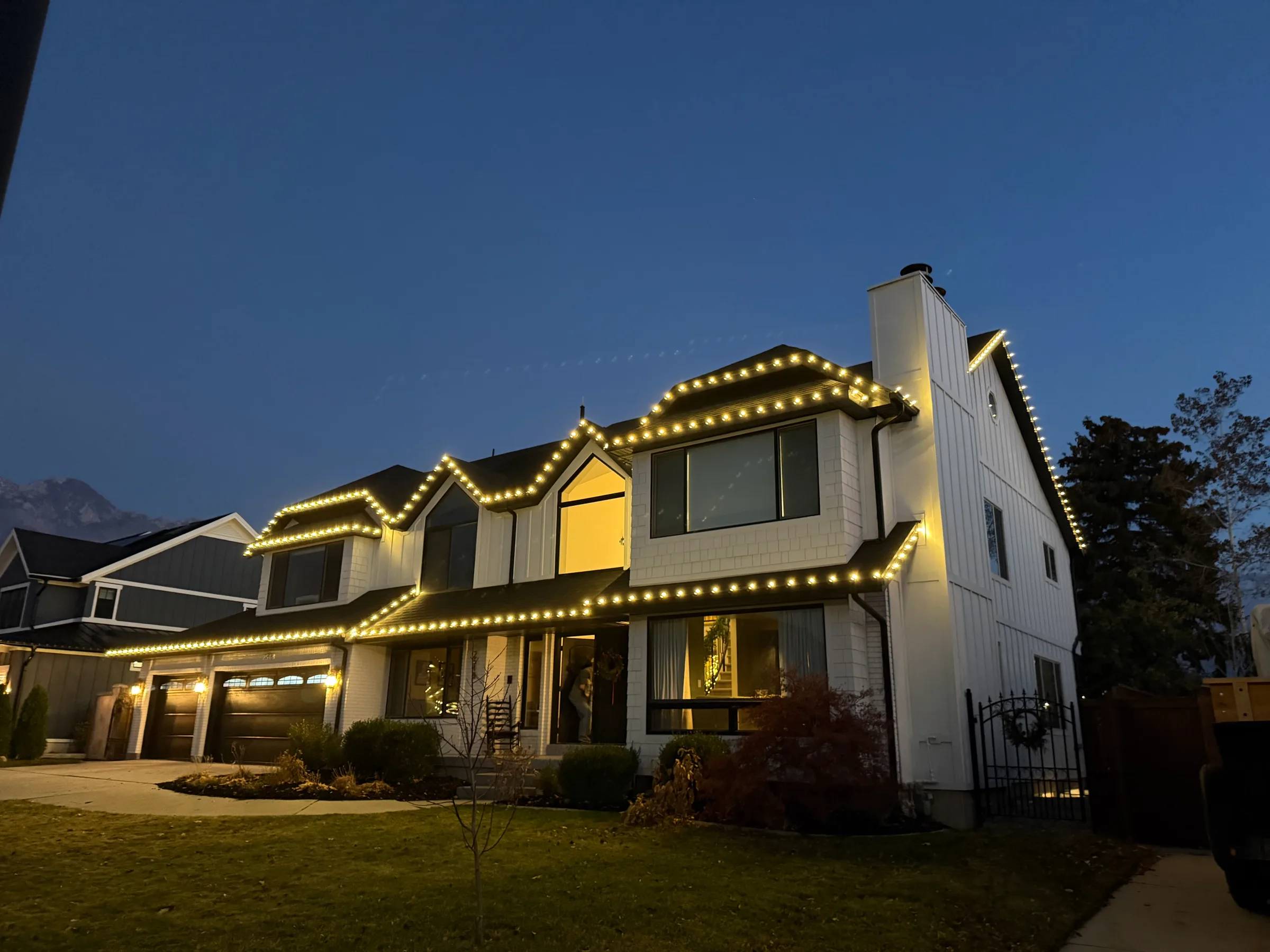 Two-story home with warm roofline lights, seen from the corner