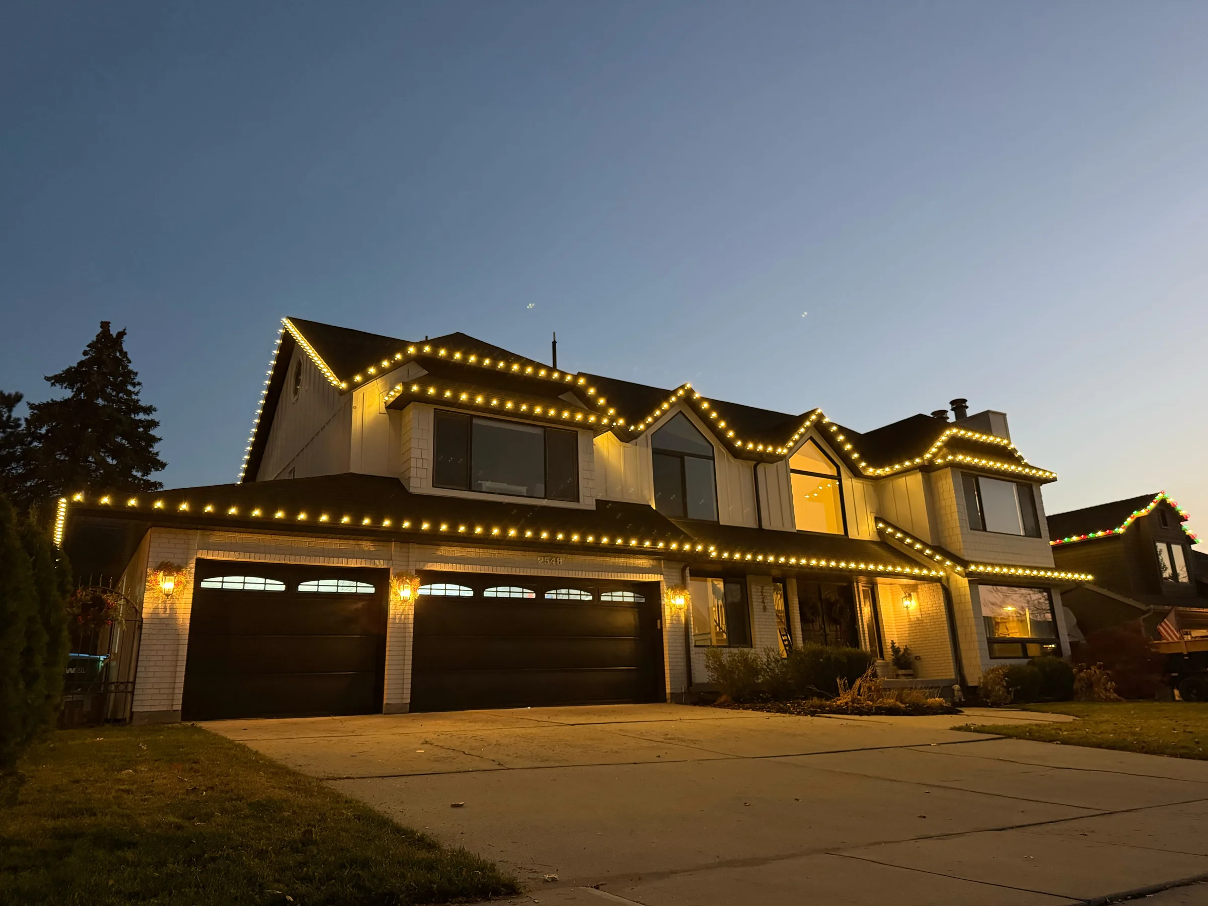 Two-story home with warm roofline lights over a three-car garage