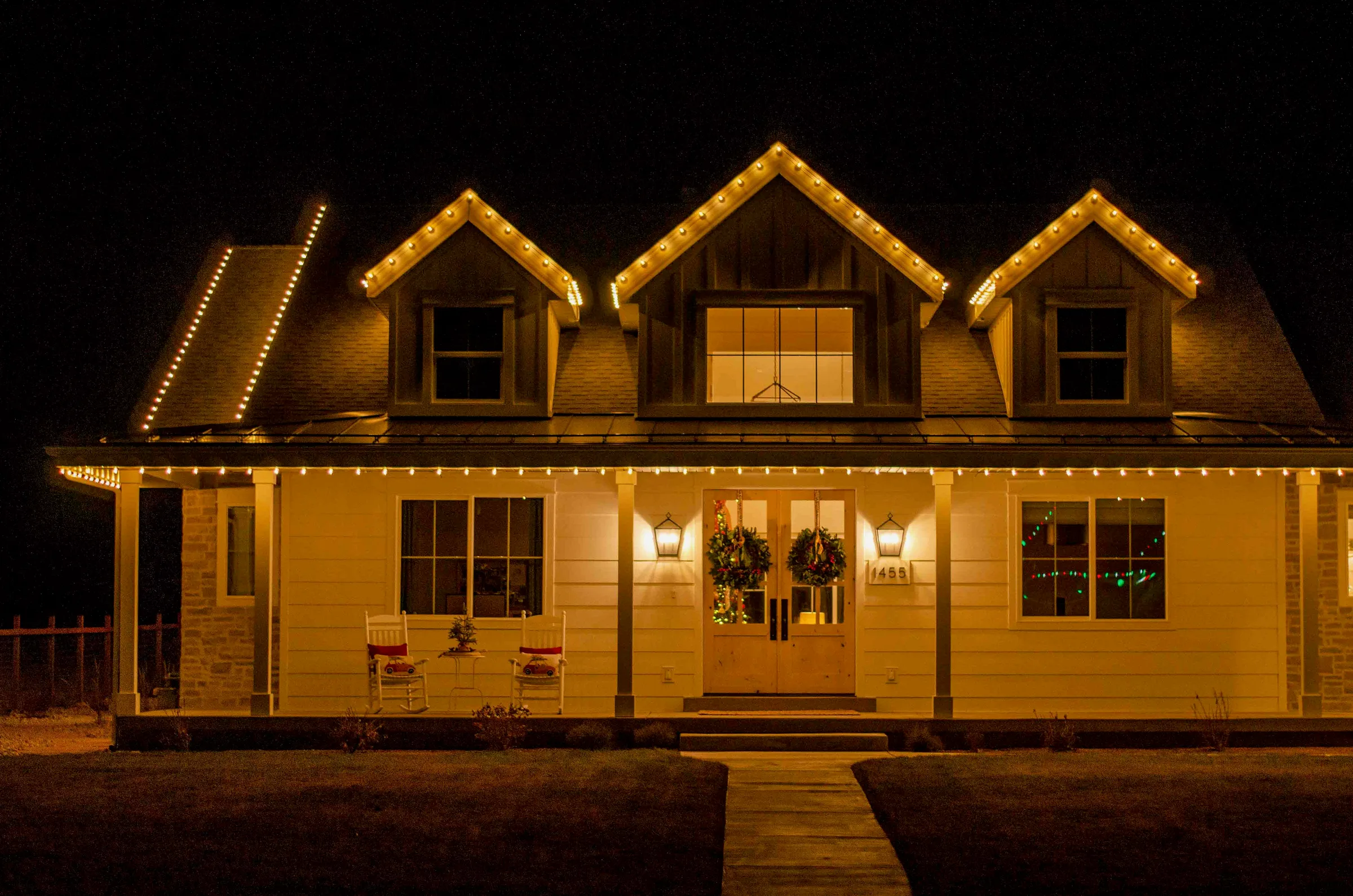 Farmhouse porch and three dormers outlined in warm white