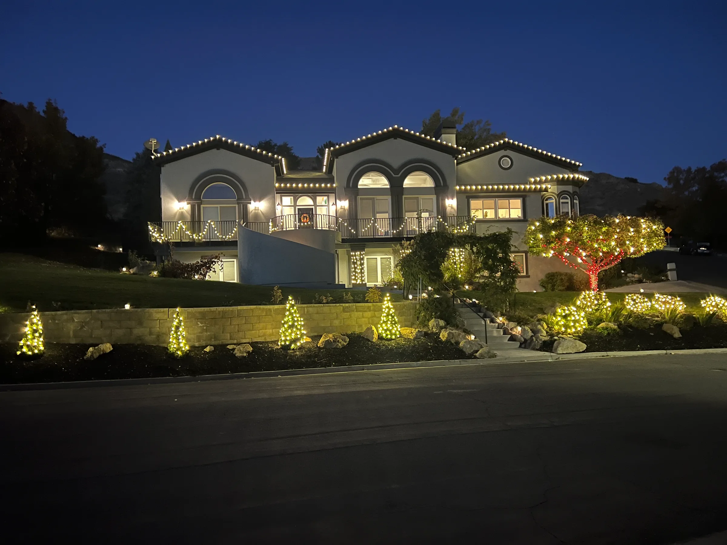 Hillside home with arched windows, lit rooflines and wrapped trees