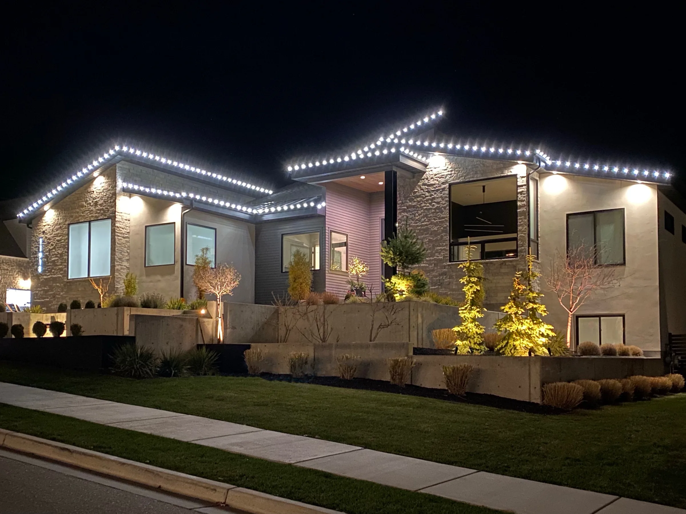 Modern stone home with white rooflines and uplit landscaping