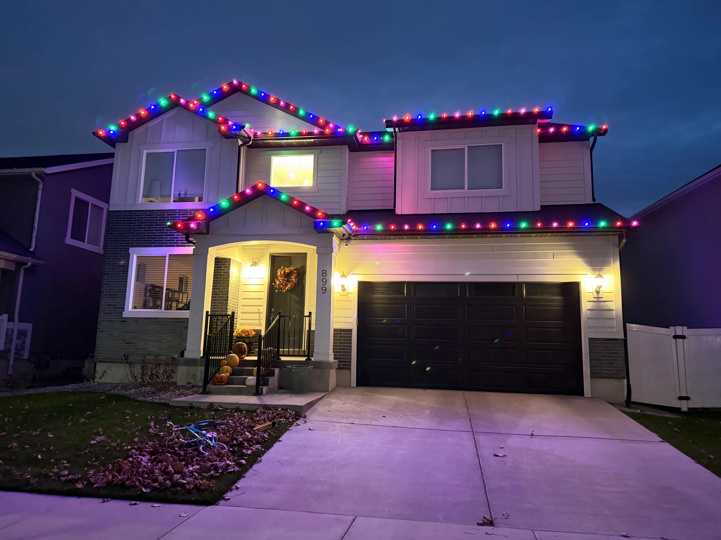 Two-story home with multicolour roofline lights at dusk