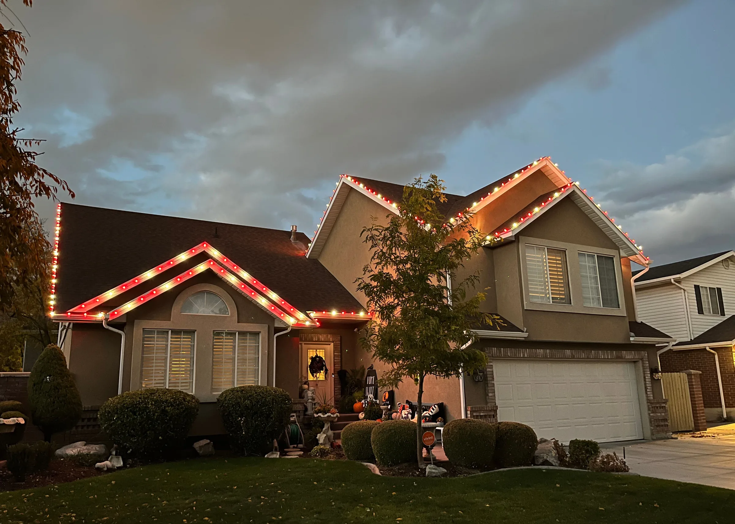 Two-story home with red and white roofline lights at dusk