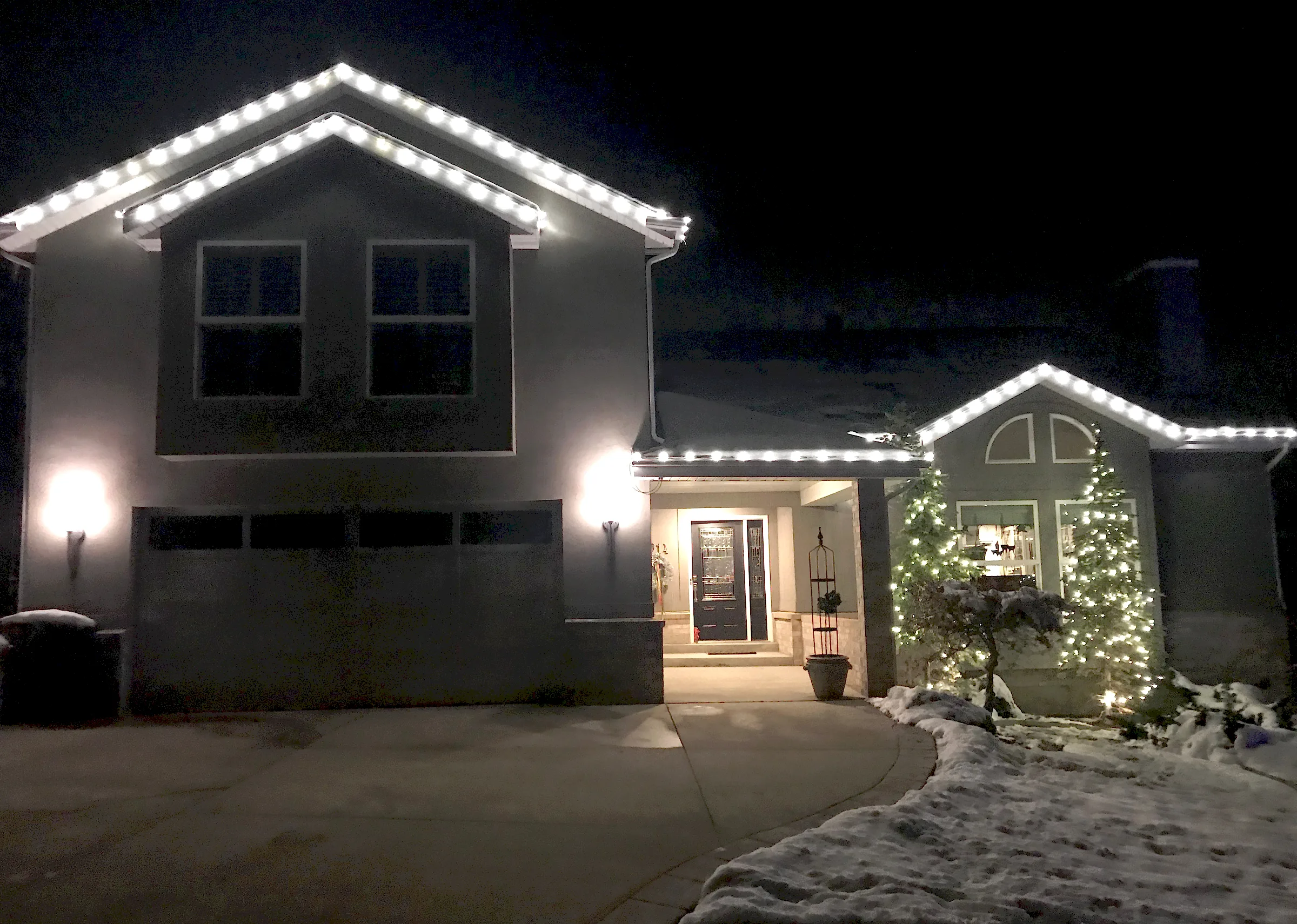 Lit rooflines and a wrapped evergreen by a snowy entry