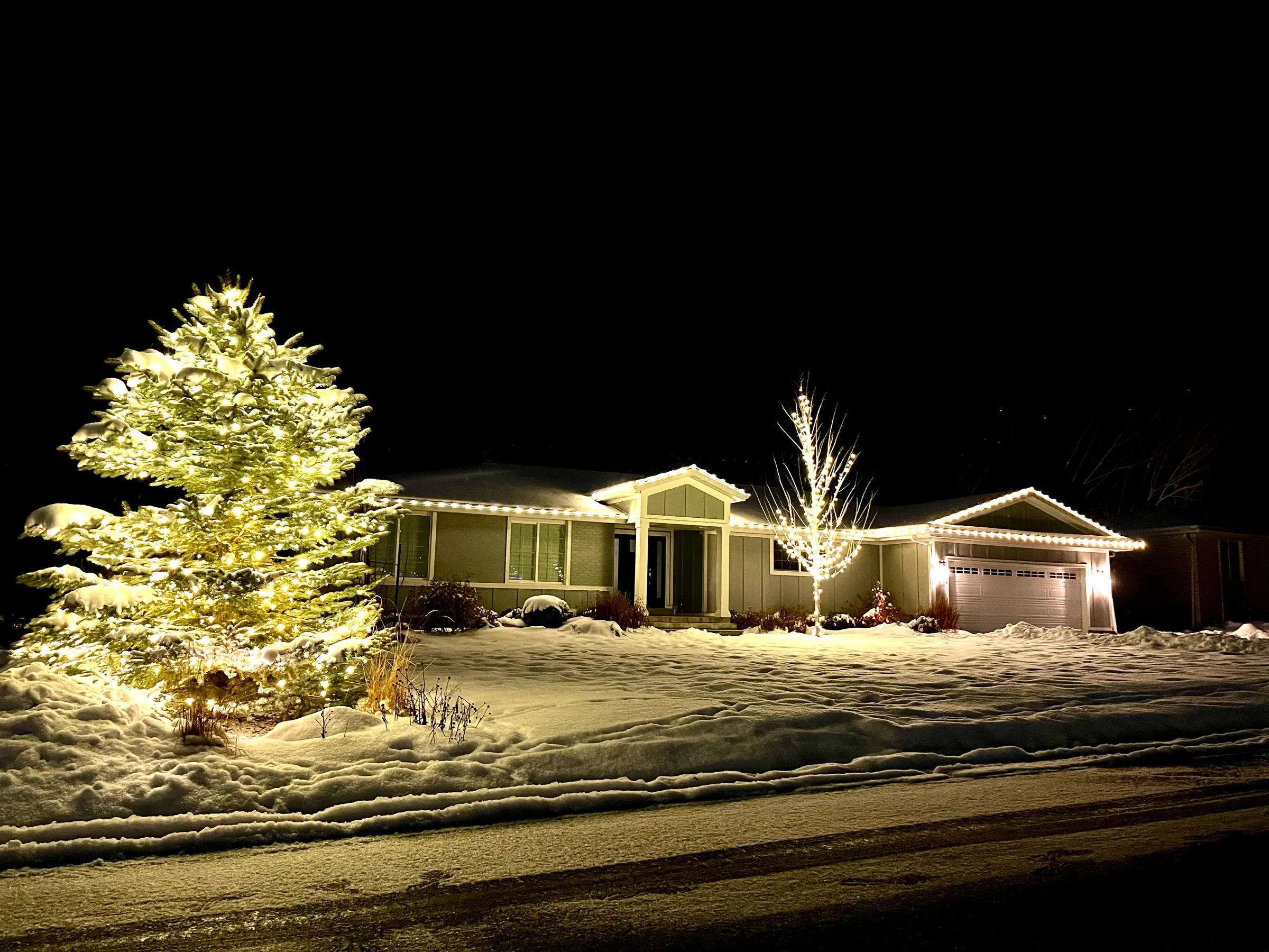 Ranch home in warm white with a lit evergreen in the snow