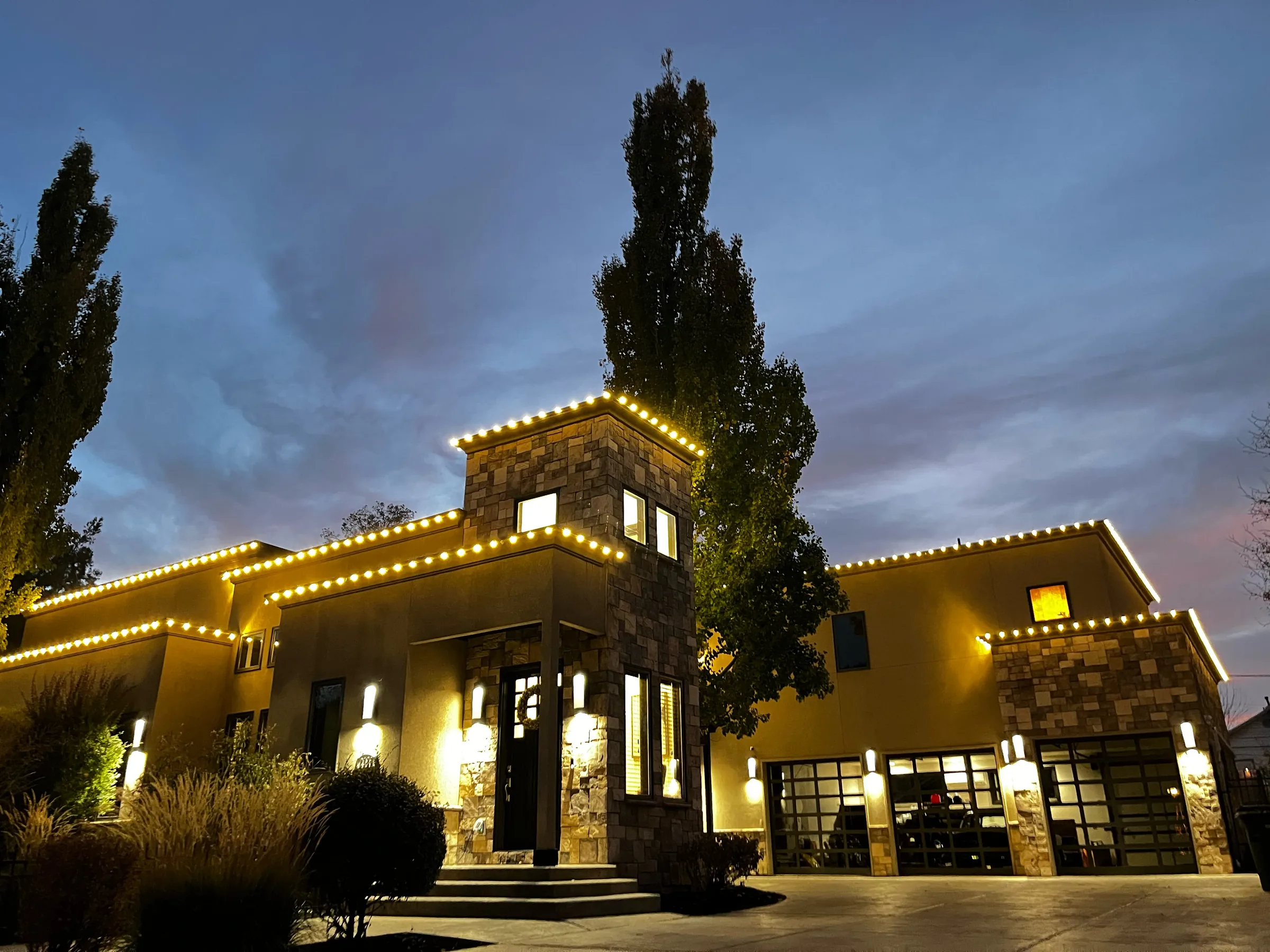 Stone home with warm roofline lighting at dusk