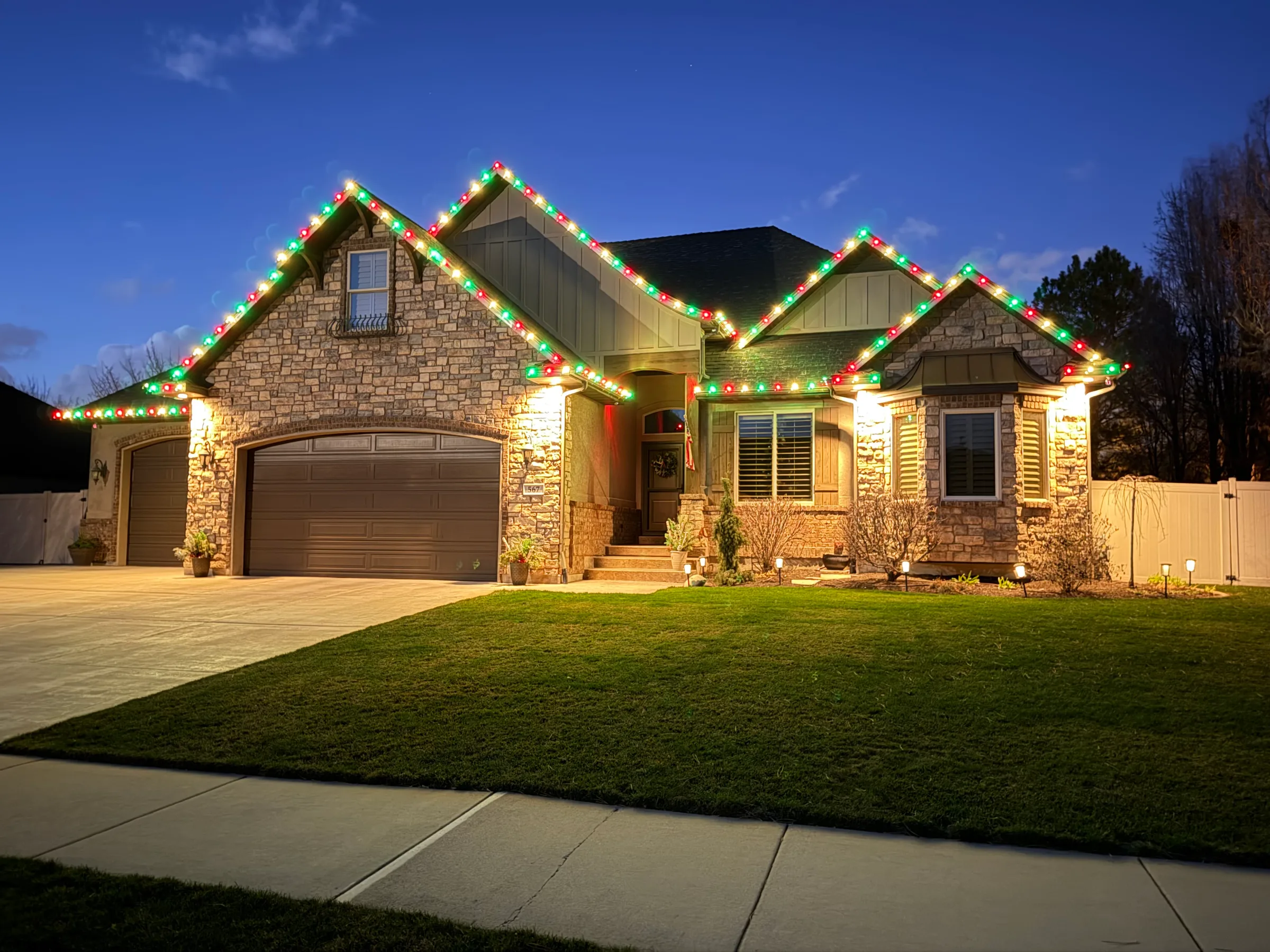 Stone home with red and green lights on every gable at dusk