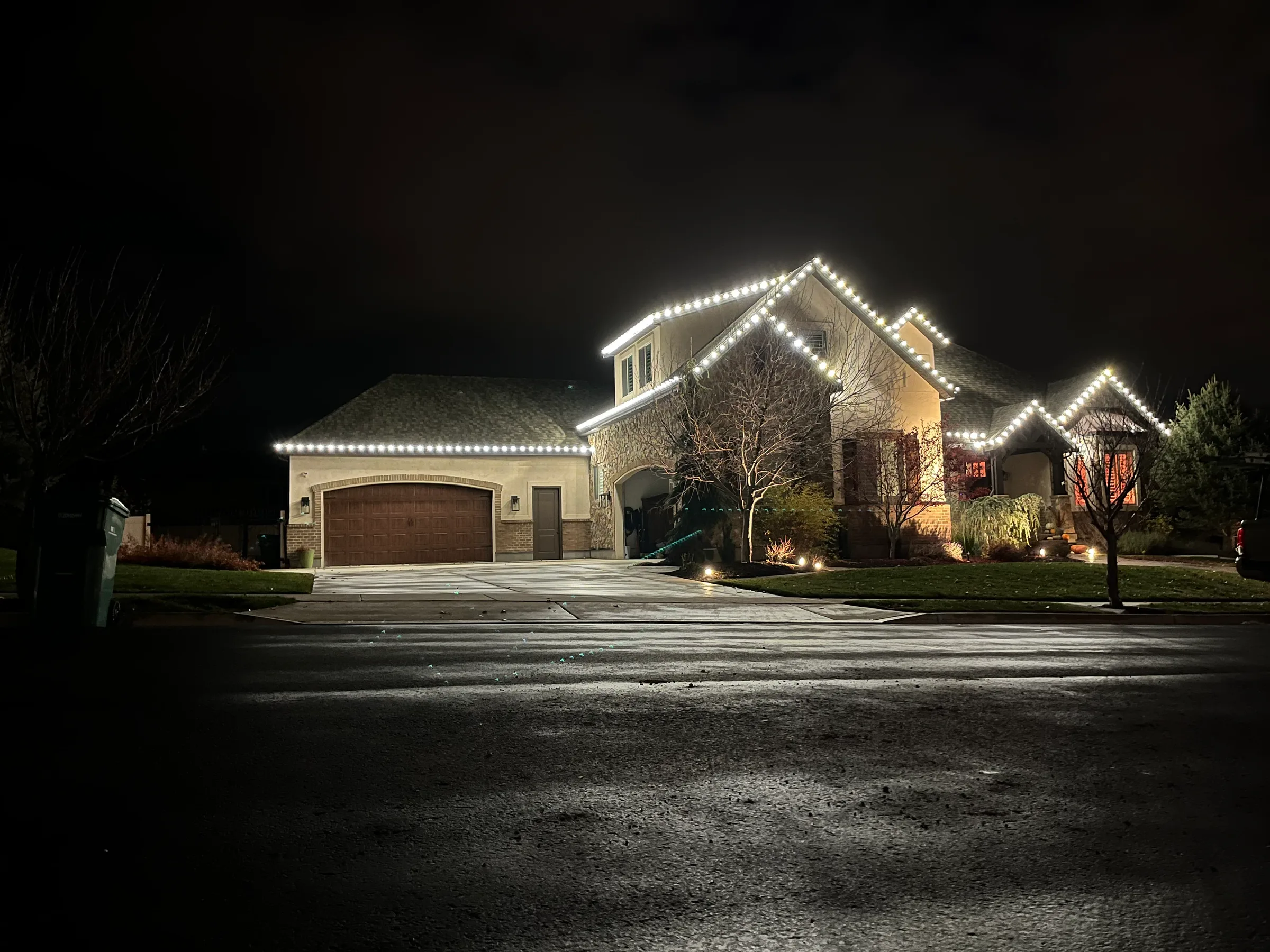 Stucco home with white roofline lights over a rain-wet street